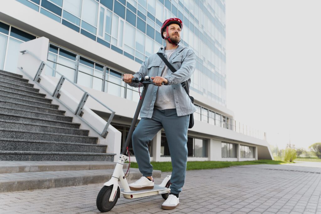 Man riding a fast speed e scooter of classic colours white and black. He has a helmet on for protection, in addition to a cross shoulder bag.