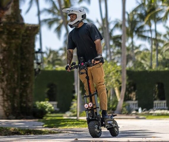 A man wearing a protective helmet and casual clothing is riding a Confasion T88 Plus on a smooth pathway, with tall palm trees and greenery in the background, enjoying a sunny day outdoors