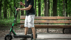 A man standing with an off-road e scooter in a forest park, showing its durable design for outdoor rides, rough terrain, and nature trails.