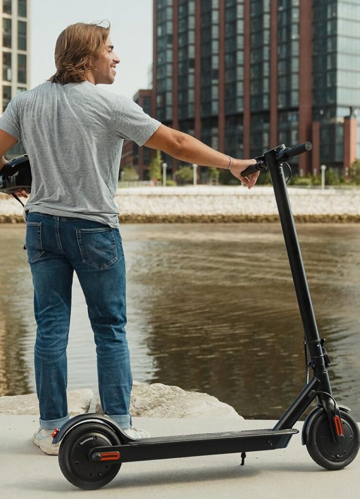 A man standing with the Hover-1 Journey Max by the riverside, recognized as one of the best e scooters for hills with strong build and dependable performance.