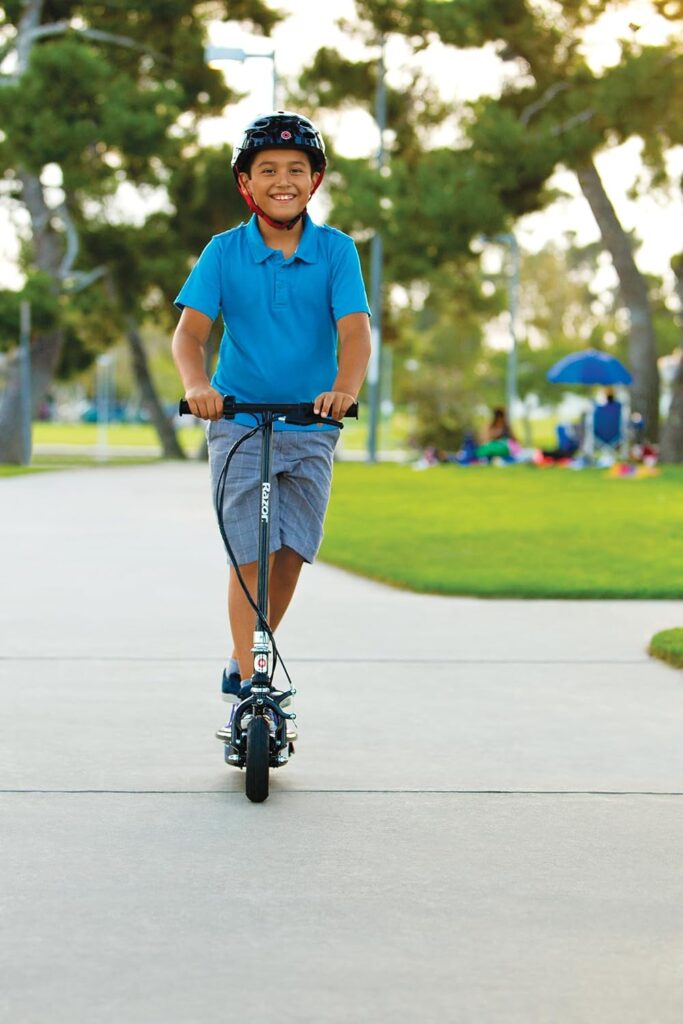 A boy riding a Razor E100 Glow electric scooter on a park pathway, wearing a helmet, enjoying its lightweight design and child-friendly features.