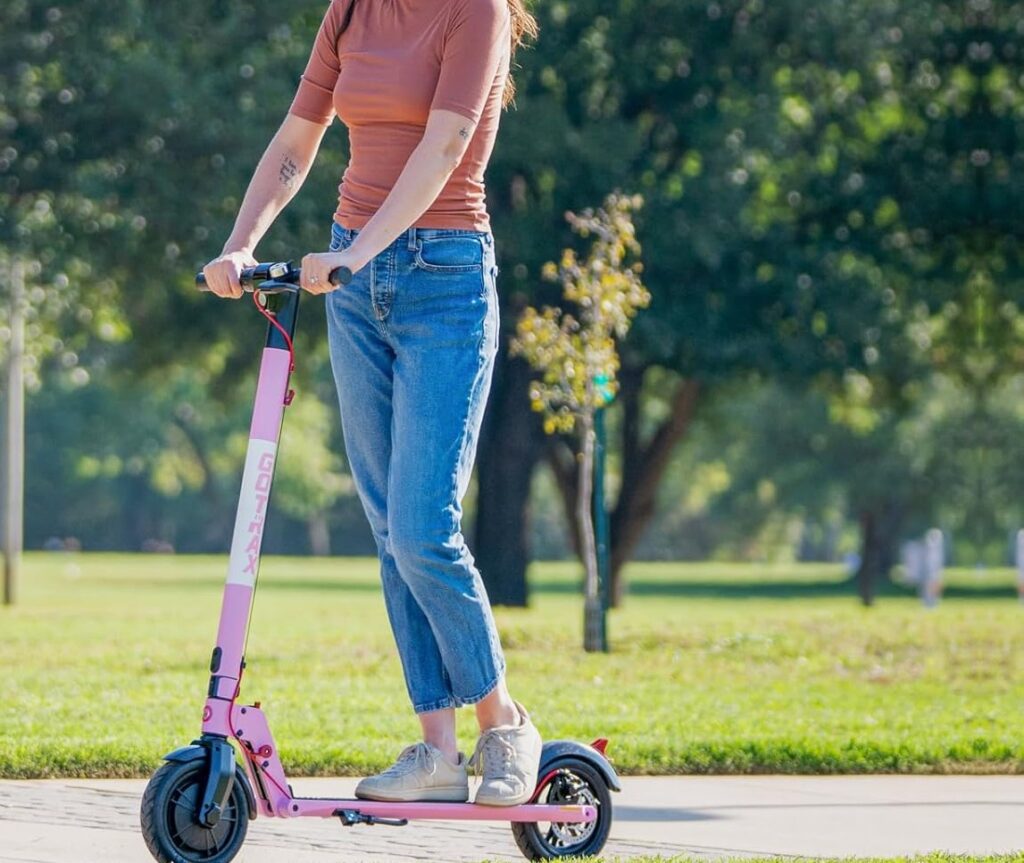 A woman riding a pink GOTRAX electric scooter in a park on a sunny day, showcasing one of the best e scooters under 500$.