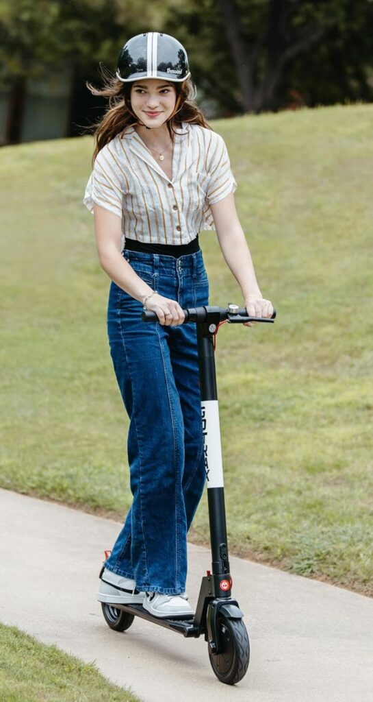 A young woman wearing a helmet rides an electric scooter on a park pathway, smiling while enjoying a safe ride.