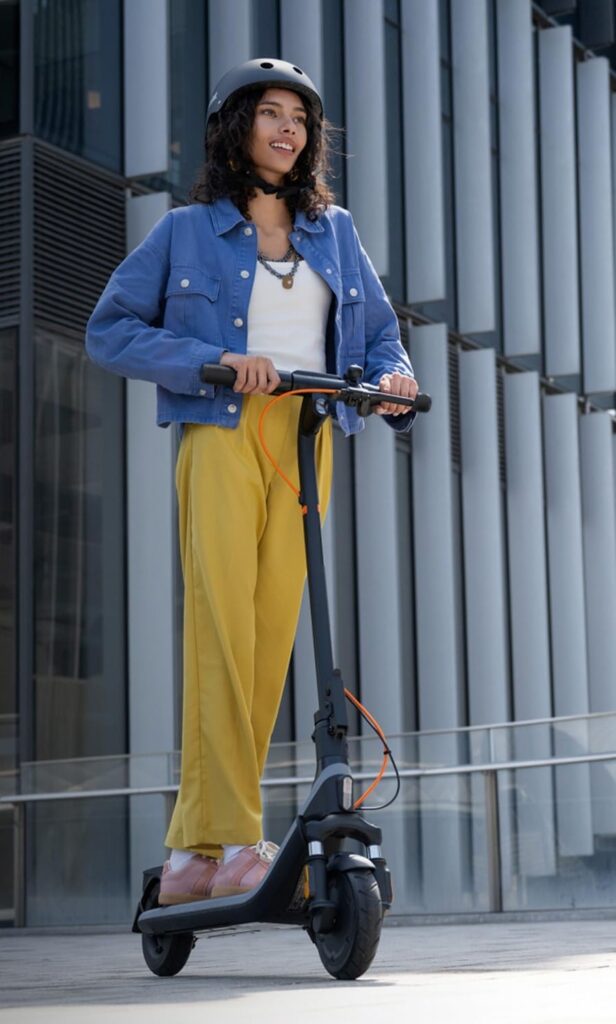 A woman in a blue jacket and yellow pants rides the best electric scooter under $300 in an urban setting, enjoying a smooth commute with safety gear.