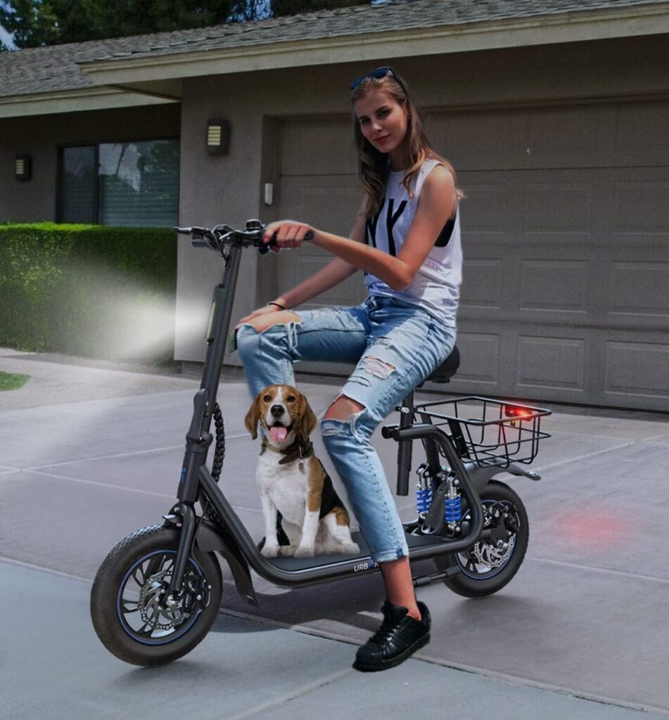 A woman sitting on an Urban Max C1 seated electric scooter with a beagle dog on the footrest, parked in front of a house; ideal for relaxed suburban rides with pets.