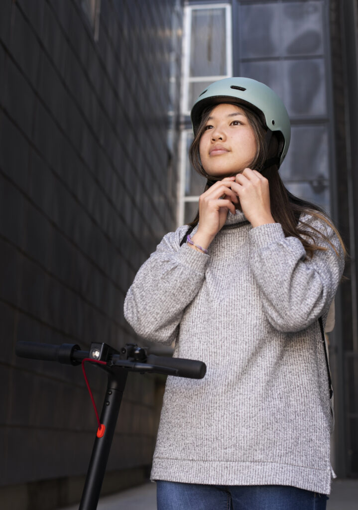 A young woman adjusts her helmet before riding an electric scooter, emphasizing the importance of wearing protective gear to reduce the risk of head injuries and ensure safe commuting.