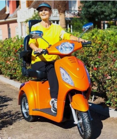 Senior woman riding an orange electric mobility scooter outdoors, enjoying independent and comfortable mobility on a sunny day.