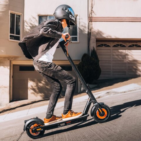 A person wearing a black helmet rides an e-scooter for heavy adults up a steep residential hill on a sunny day.