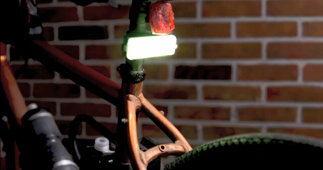 A bright rear LED safety light mounted on a bicycle seat post in front of a brick wall at night.