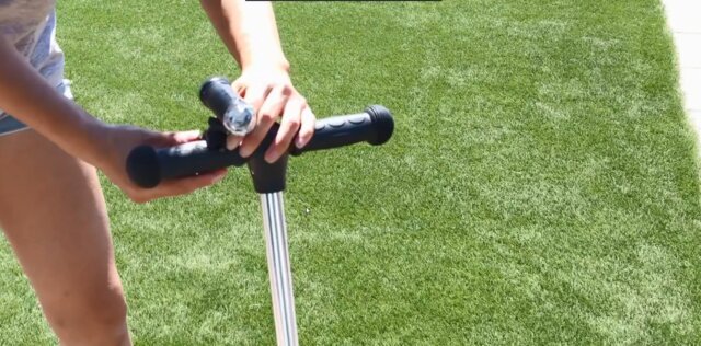 Close-up of hands adjusting the front light on a scooter handlebar while standing on green grass