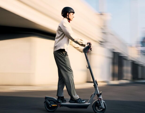 A rider balances on one leg on the best segway electric scooter, the Segway E3 Pro, while another rider watches from behind under a bright blue sky.