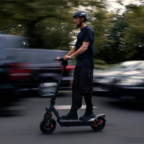 Man riding a Segway-style electric scooter on a city street with motion-blurred cars in the background; a best segway e scooter choice for urban commuting.