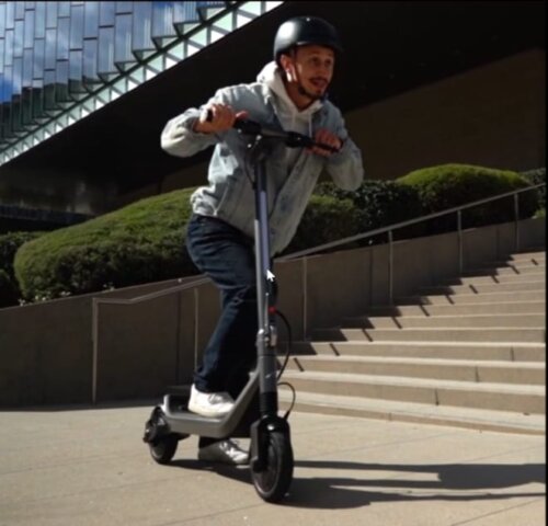A rider on an electric scooter glides down a tree-lined pathway in a park on a sunny day, showcasing the best lightweight e scooter for a smooth, eco-friendly outdoor ride.