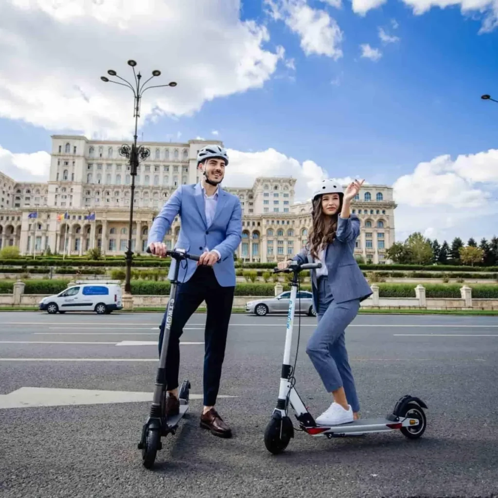 Two helmeted riders pose on electric scooters in front of a large historic building under a bright blue sky, showcasing the best lightweight e scooter for stylish urban commuting.